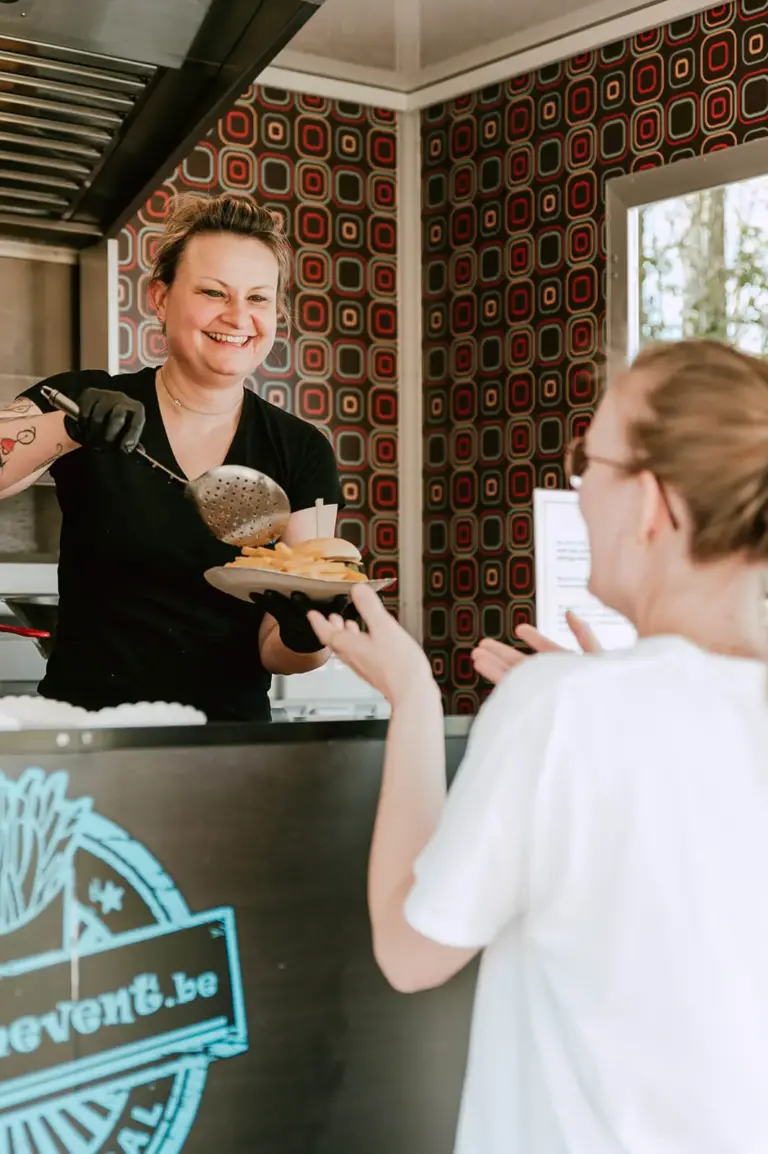 Medewerkster van MTM Event serveert een hamburger vanuit de foodtruck